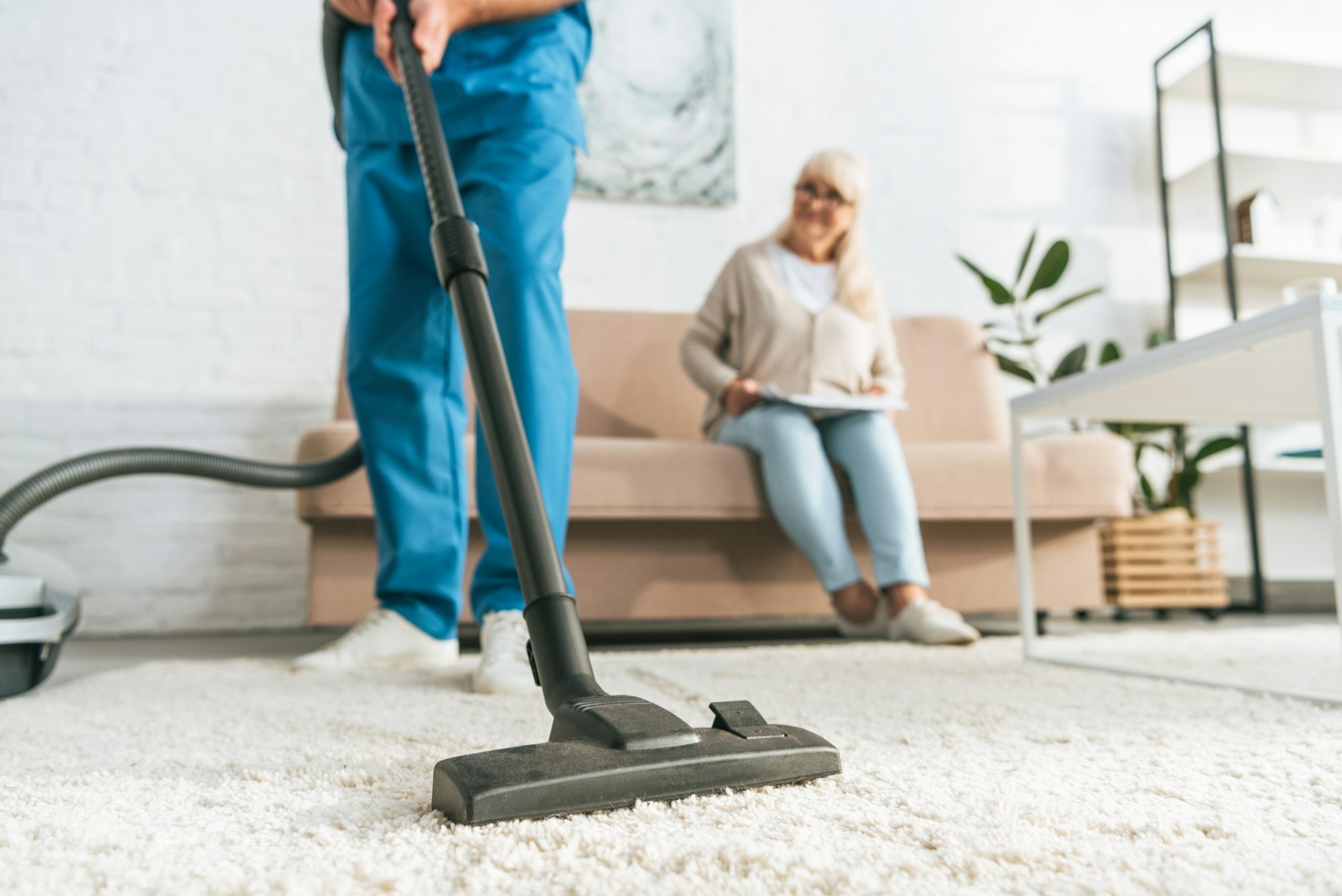 cropped shot of man using vacuum cleaner while senior woman sitting on sofa