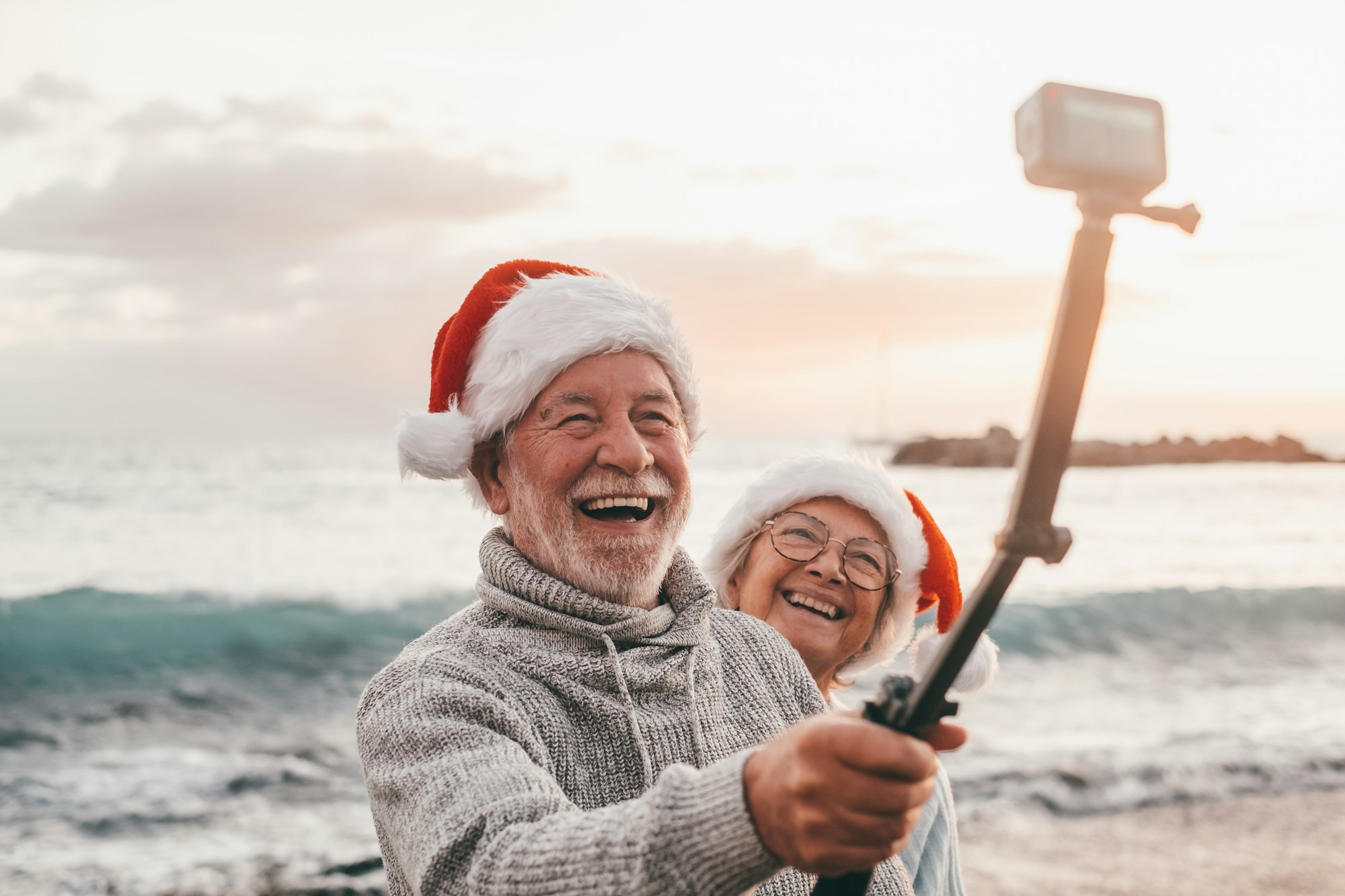 Portrait of two cute old persons having fun and enjoying together at the beach on christmas days