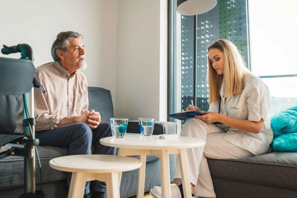 Senior man and his caregiver, young woman, sitting on the couch at his apartment