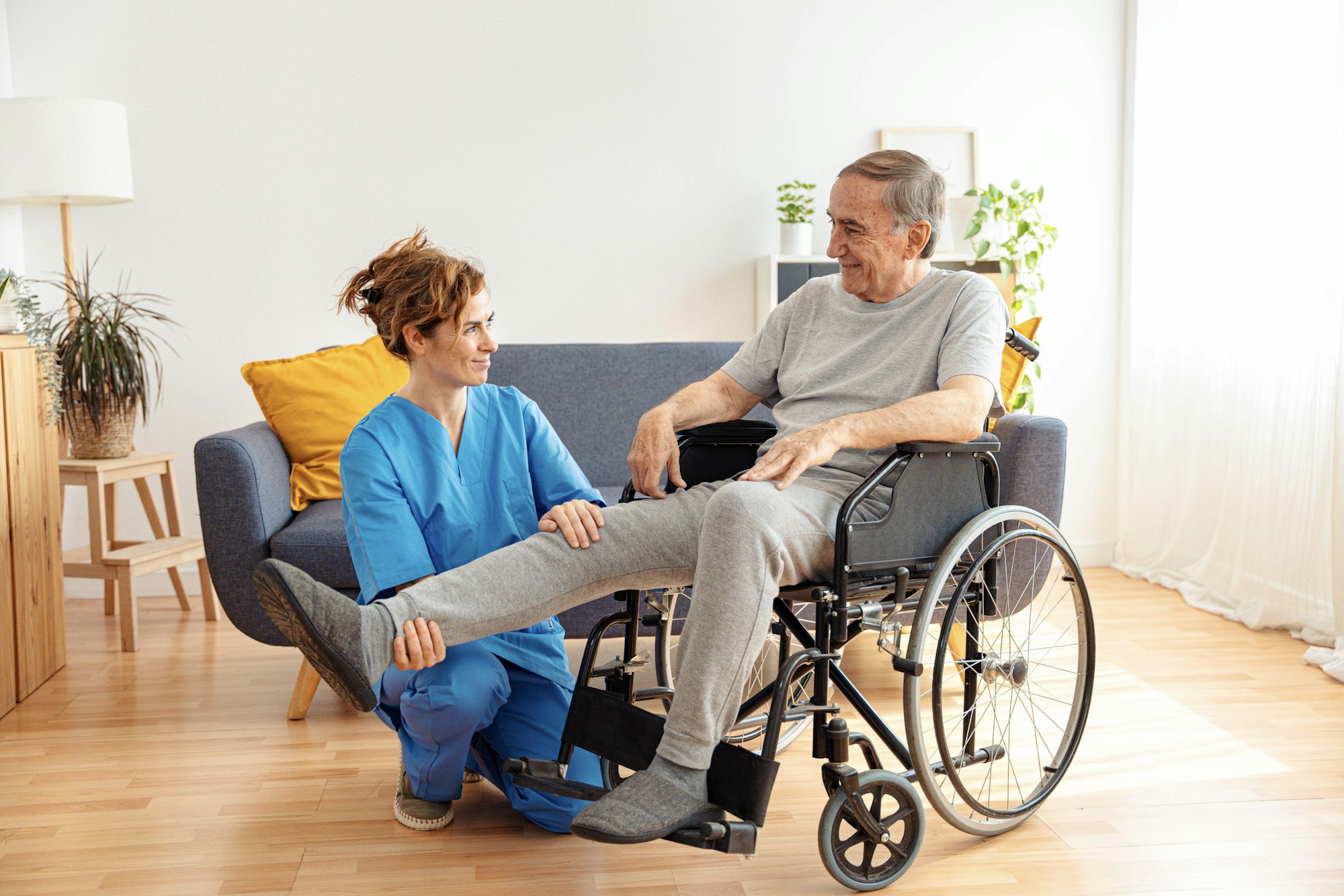 Young caregiver assisting senior man in wheelchair indoors